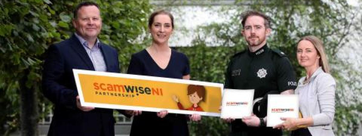 Four adults posing with three Scamwise NI props.