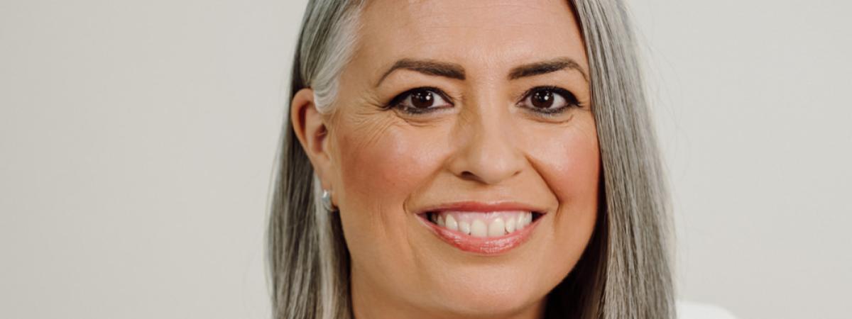 Lady wearing white jacket with black top, grey hair styled in a bob.